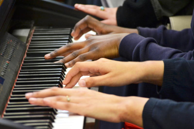 Multiple hands on a piano keyboard