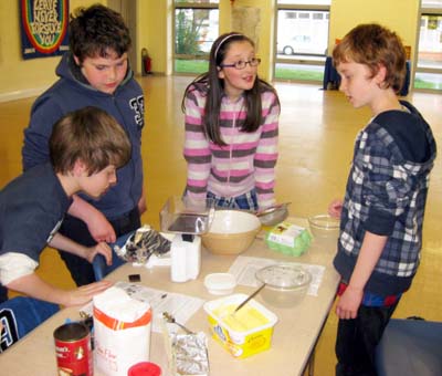 Young people standing around a table with food and kitchen equipment
